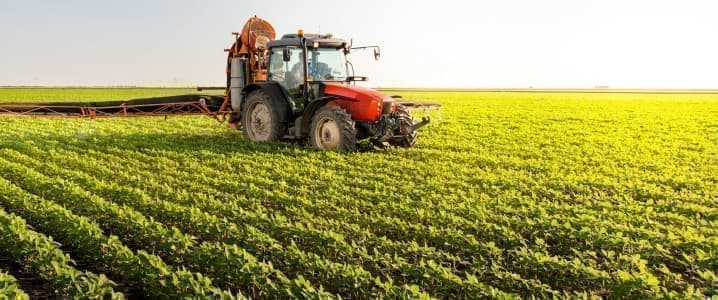 A tractor driving across a field fertilizing crops.
